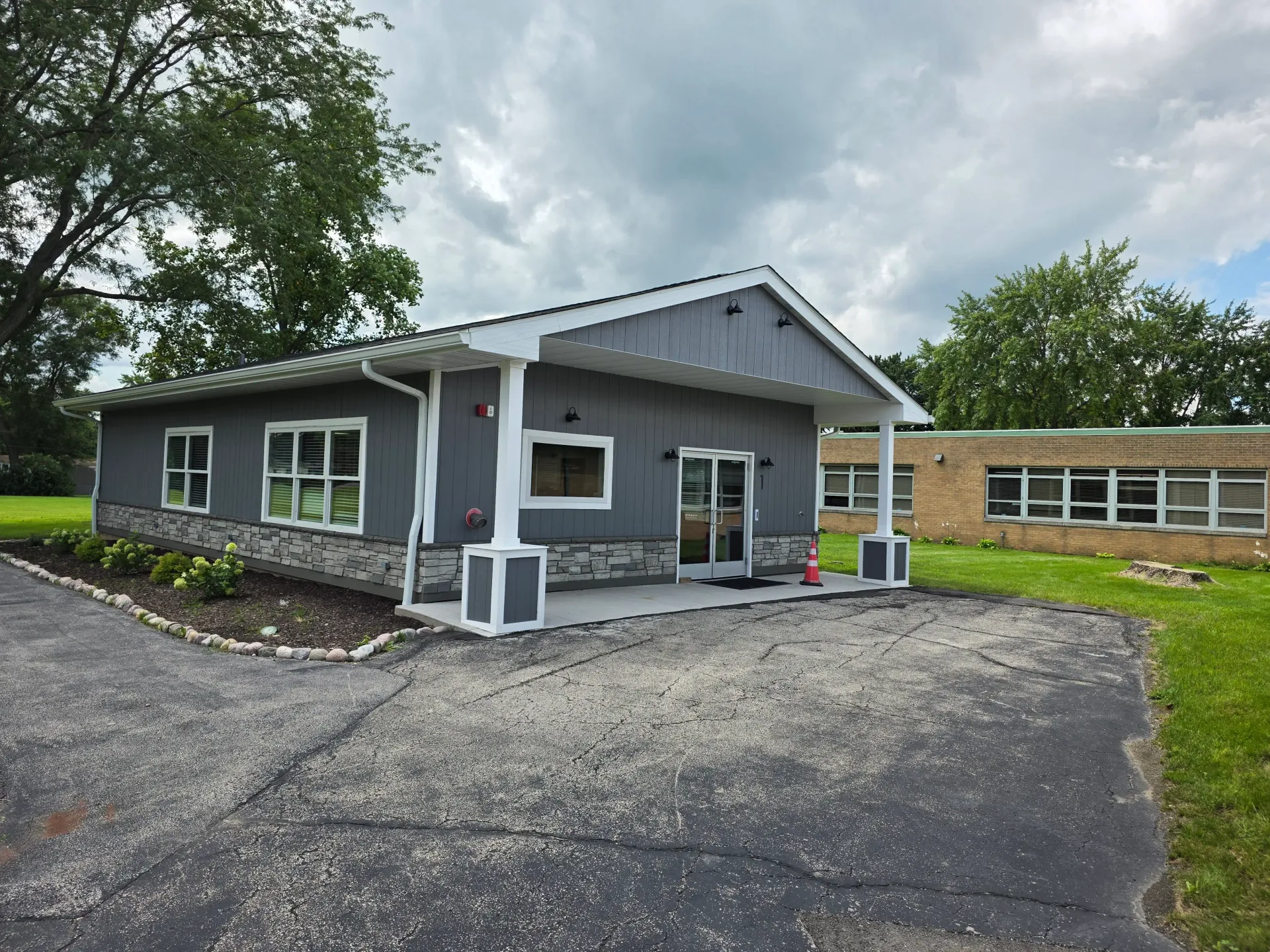 Gray commercial building with white-framed windows and a landscaped entrance.